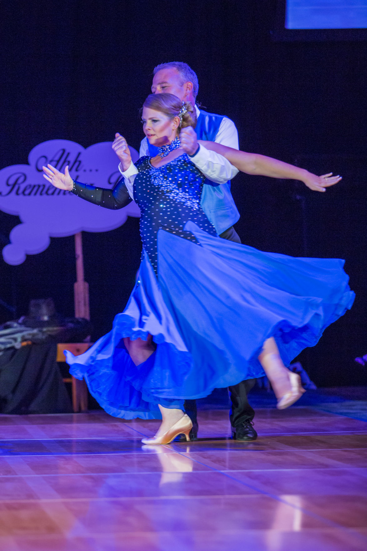 Blue-lit black drape backdrop behind ballroom dancers at charity event