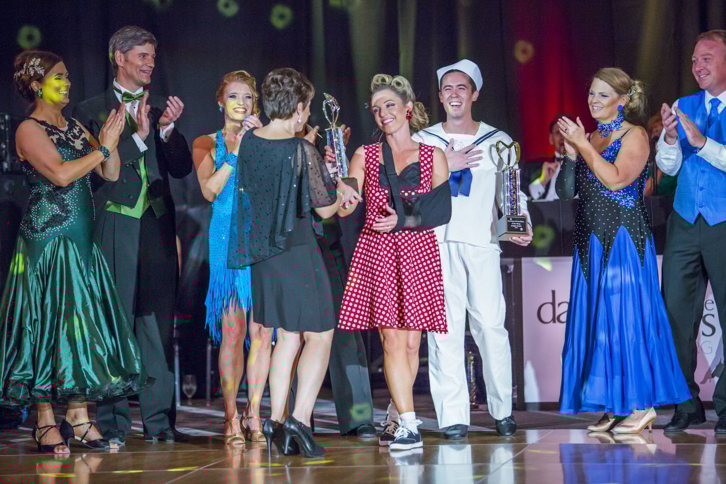 Full stage with black drape wall behind performers at charity dance event